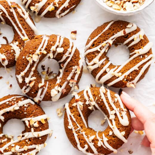 A hand holding a pumpkin donut with coconut-maple glaze.