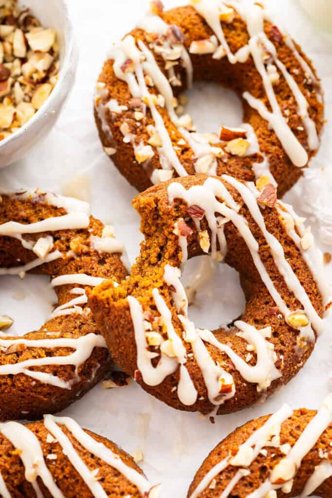 Pumpkin donuts scattered on a surface. One has a bite taken out of it.